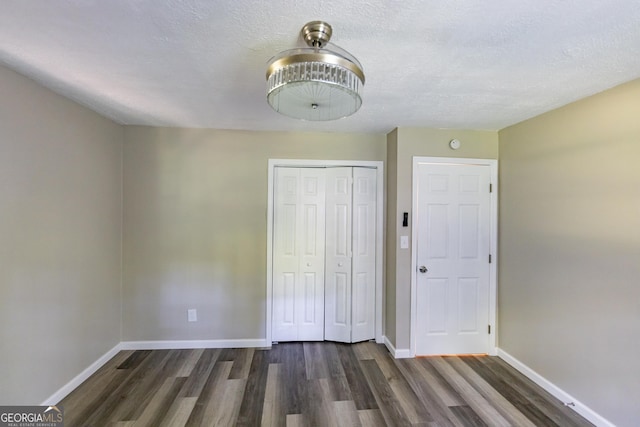 unfurnished bedroom featuring dark wood-style floors, a closet, a textured ceiling, and baseboards