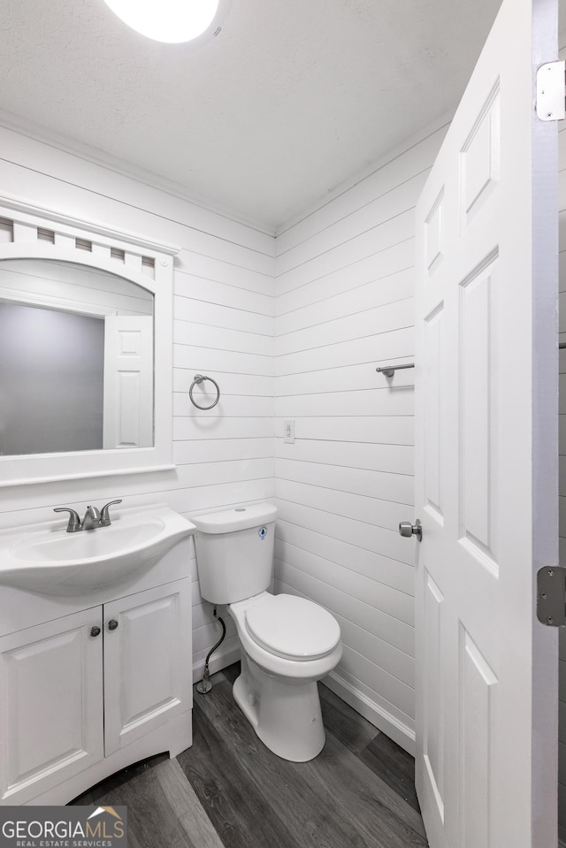bathroom with vanity, wood walls, wood finished floors, and toilet