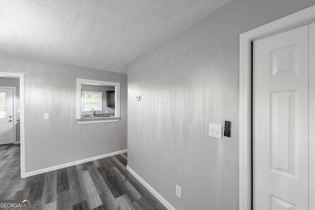 hall with a sink, a textured ceiling, baseboards, and dark wood-type flooring