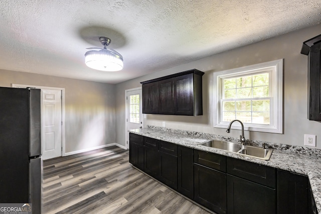 kitchen with wood finished floors, a sink, baseboards, freestanding refrigerator, and light stone countertops