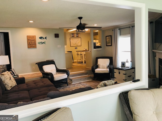 living room with crown molding, ceiling fan, a fireplace, and hardwood / wood-style floors