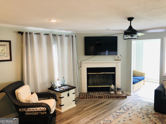 living room with crown molding, wood-type flooring, a brick fireplace, and a textured ceiling