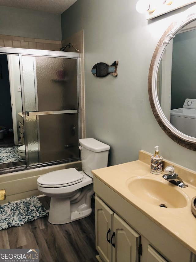 full bathroom with bath / shower combo with glass door, washer / dryer, hardwood / wood-style flooring, vanity, and toilet