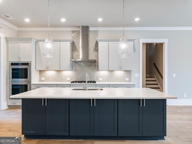 kitchen with stainless steel appliances, white cabinetry, a kitchen island with sink, and wall chimney range hood