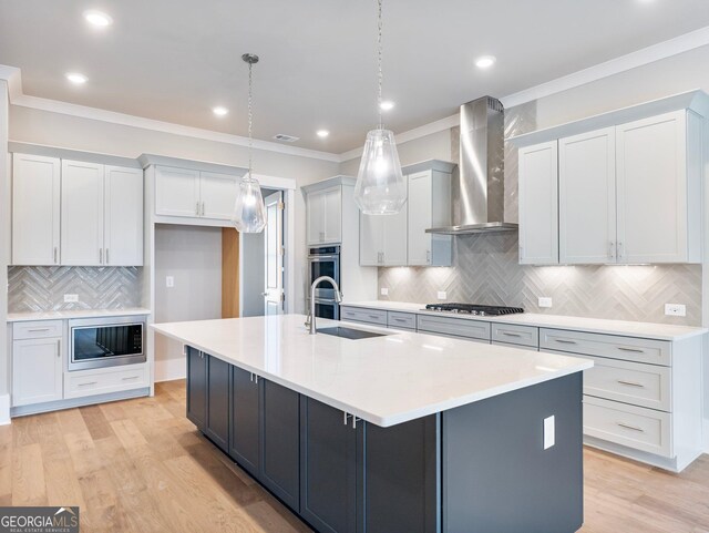 kitchen featuring wall chimney exhaust hood, a kitchen island with sink, hanging light fixtures, and appliances with stainless steel finishes