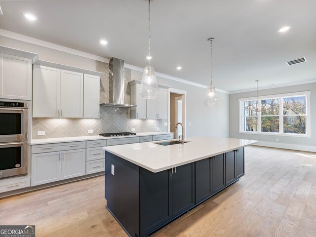 kitchen with a kitchen island with sink, sink, decorative light fixtures, and wall chimney range hood