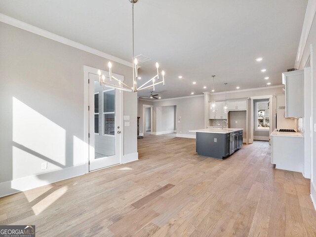 kitchen with pendant lighting, backsplash, a center island with sink, white cabinets, and light wood-type flooring