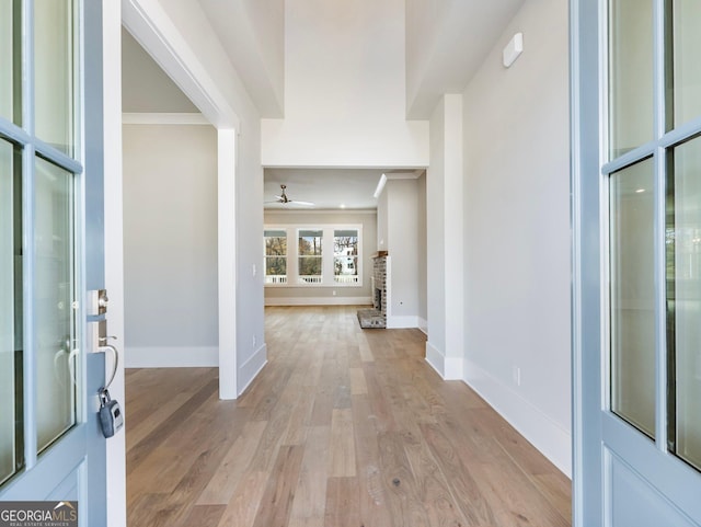 foyer entrance featuring light wood-type flooring, a stone fireplace, ceiling fan, and ornamental molding