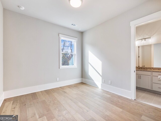 unfurnished bedroom with light wood-type flooring, ensuite bathroom, and sink