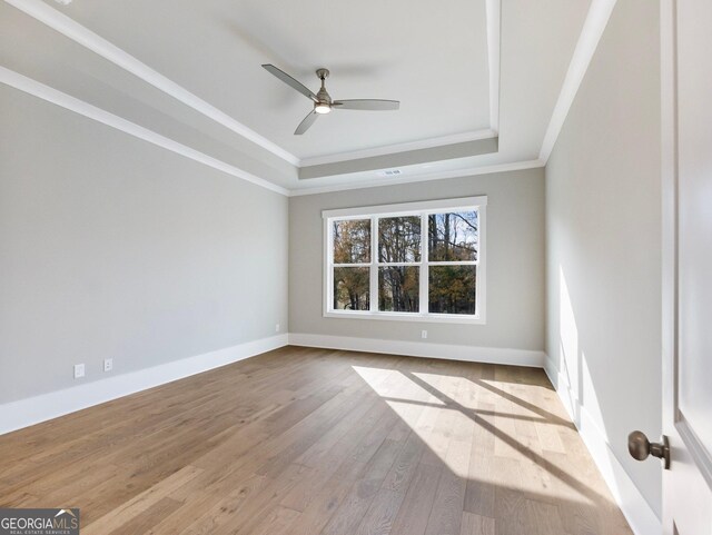 unfurnished room featuring ceiling fan, a raised ceiling, light wood-type flooring, and ornamental molding