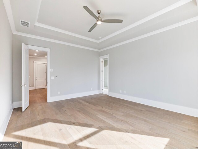 unfurnished room featuring a tray ceiling, ceiling fan, ornamental molding, and light wood-type flooring