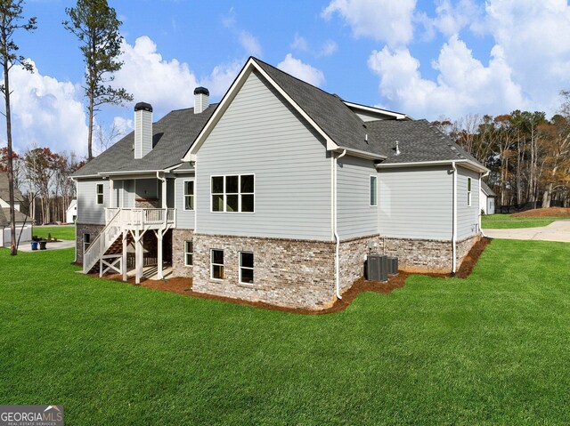 rear view of house featuring central air condition unit and a lawn