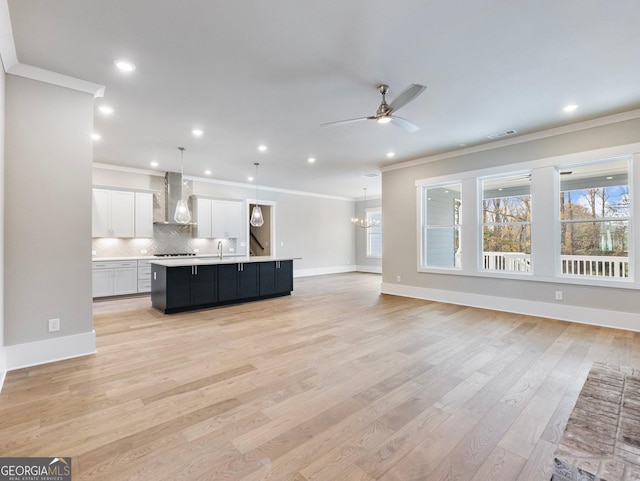 unfurnished living room with ceiling fan with notable chandelier, light hardwood / wood-style floors, sink, and crown molding