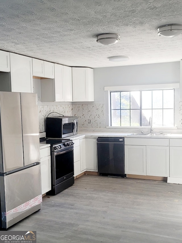 kitchen with sink, tasteful backsplash, white cabinets, black appliances, and light wood-type flooring