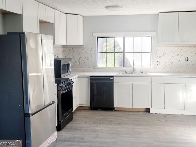 kitchen featuring white cabinetry, sink, light hardwood / wood-style floors, a textured ceiling, and black appliances