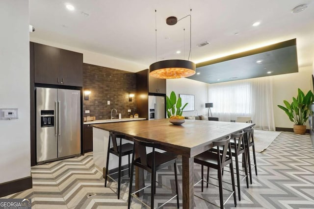 interior space featuring dark brown cabinetry, sink, high end fridge, and tasteful backsplash