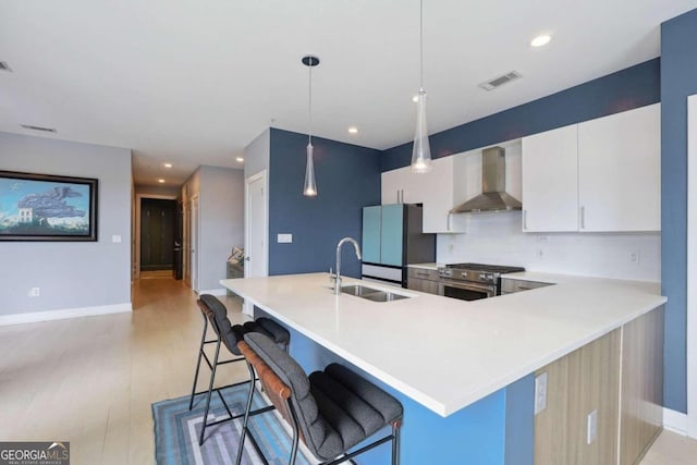 kitchen with stainless steel range, hanging light fixtures, decorative backsplash, a kitchen breakfast bar, and wall chimney exhaust hood