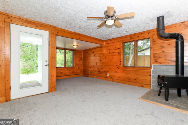 interior space with ceiling fan, a wood stove, wood walls, carpet, and a textured ceiling