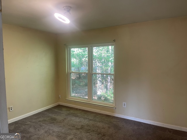 unfurnished room featuring dark colored carpet and a healthy amount of sunlight