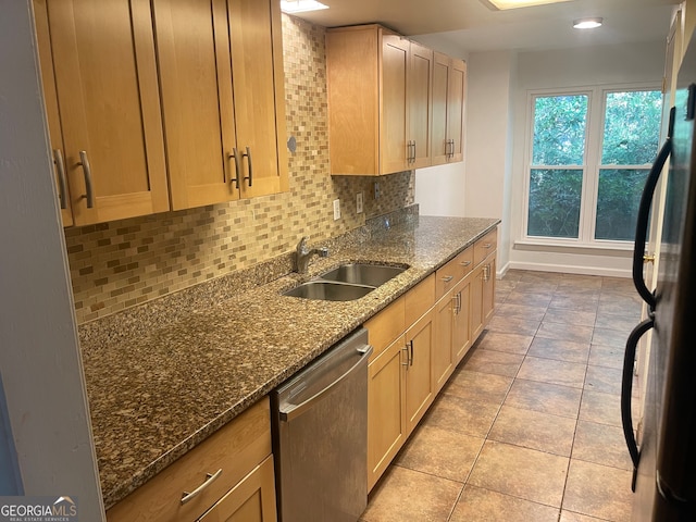 kitchen with refrigerator, stainless steel dishwasher, sink, dark stone counters, and backsplash