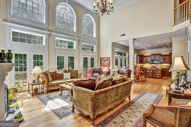 living room featuring crown molding, french doors, a chandelier, ornate columns, and a towering ceiling