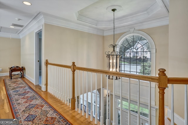 corridor with light hardwood / wood-style floors, crown molding, a raised ceiling, and a chandelier