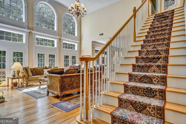 stairs featuring french doors, an inviting chandelier, hardwood / wood-style floors, a towering ceiling, and ornamental molding