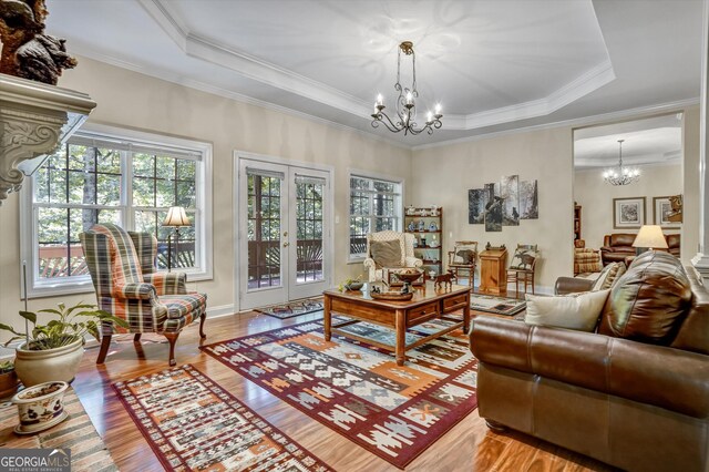 living room with ornamental molding, light hardwood / wood-style flooring, a raised ceiling, and a notable chandelier