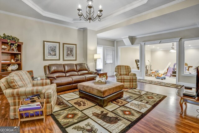 living room with a tray ceiling, wood-type flooring, ornamental molding, and a notable chandelier