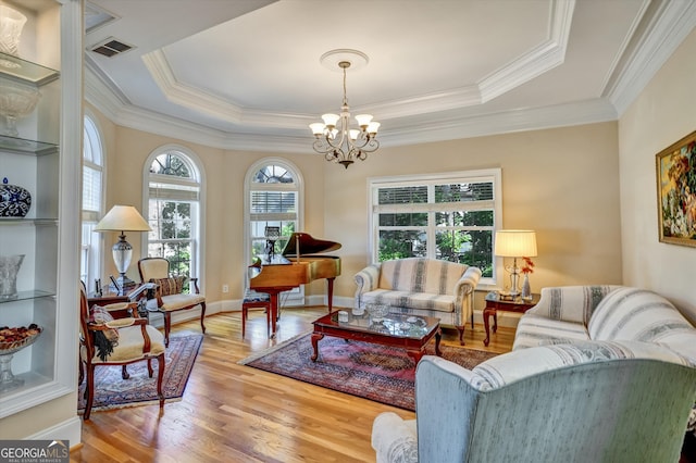 living room with ornamental molding, light wood-type flooring, a raised ceiling, and a chandelier