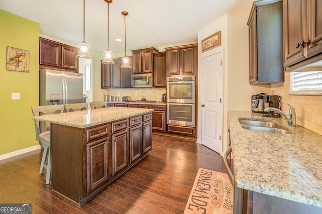 kitchen with light stone counters, dark hardwood / wood-style flooring, a kitchen island, appliances with stainless steel finishes, and sink