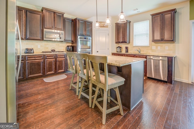 kitchen featuring tasteful backsplash, stainless steel appliances, hanging light fixtures, a center island, and dark hardwood / wood-style flooring