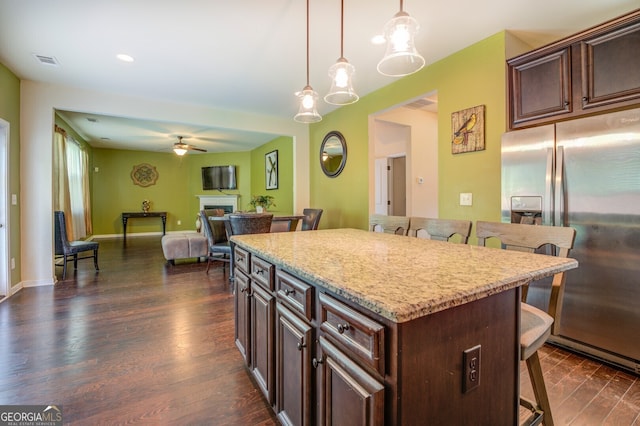 kitchen with ceiling fan, hanging light fixtures, stainless steel fridge with ice dispenser, dark hardwood / wood-style floors, and a breakfast bar