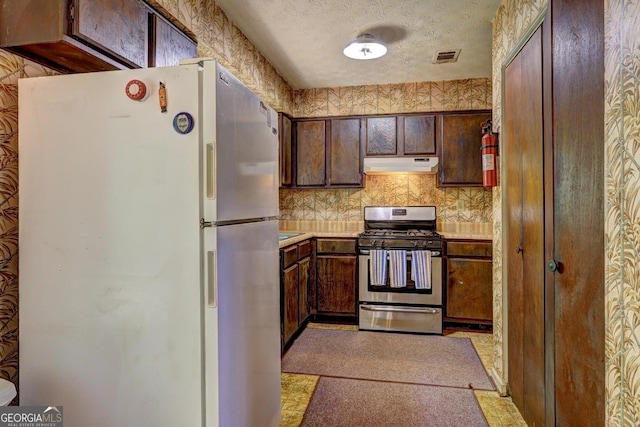 kitchen with white refrigerator, dark brown cabinetry, gas stove, and a textured ceiling