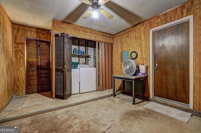 clothes washing area with wood walls, light colored carpet, a textured ceiling, ceiling fan, and washer and clothes dryer