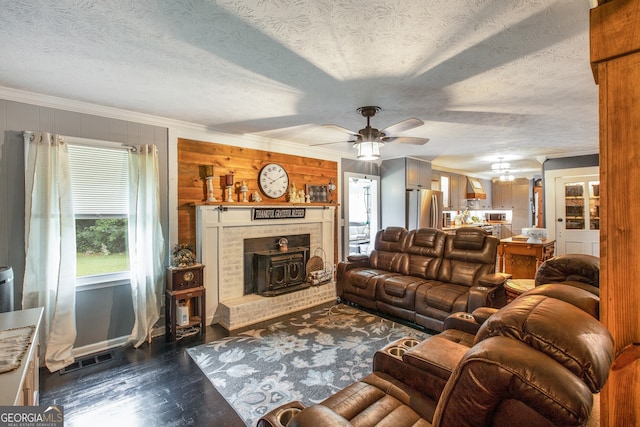 living room featuring crown molding, a textured ceiling, a brick fireplace, ceiling fan, and dark wood-type flooring