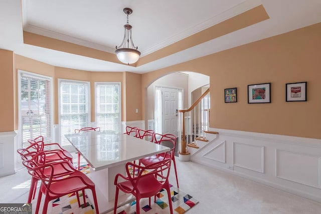 dining space with a raised ceiling, light colored carpet, ornamental molding, and plenty of natural light