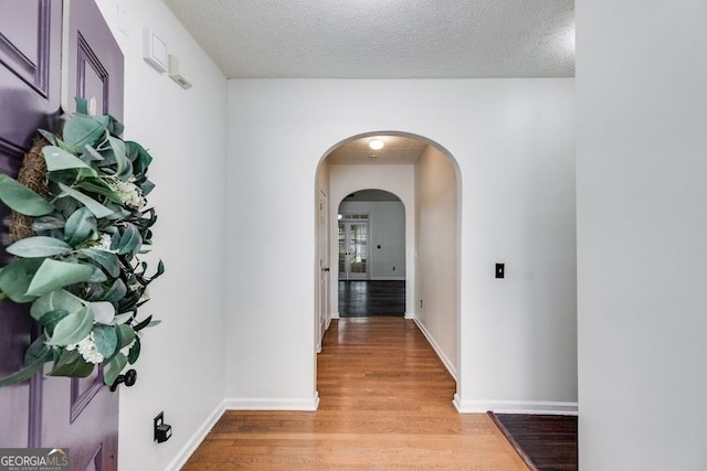 hall featuring light wood-style floors, baseboards, arched walkways, and a textured ceiling