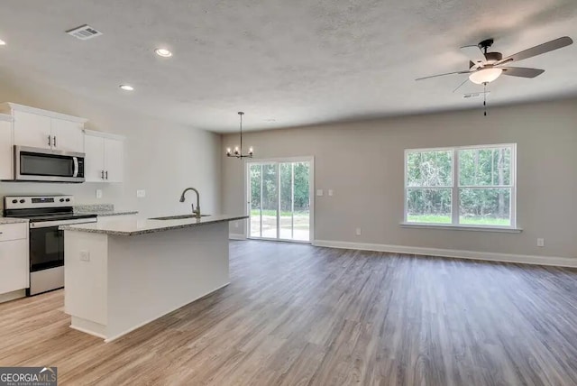 kitchen featuring pendant lighting, a kitchen island with sink, white cabinetry, stainless steel appliances, and light stone counters