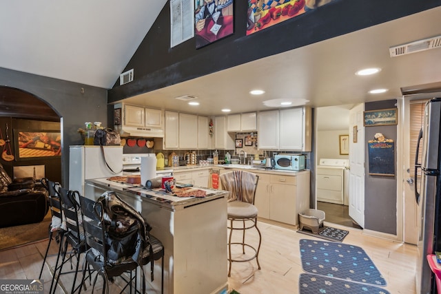 kitchen featuring washer and dryer, vaulted ceiling, sink, and light hardwood / wood-style flooring