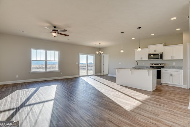 kitchen featuring white cabinetry, open floor plan, appliances with stainless steel finishes, light stone countertops, and a center island with sink