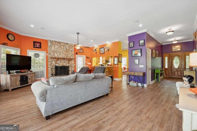 living area featuring a stone fireplace, a ceiling fan, baseboards, ornamental molding, and light wood-type flooring