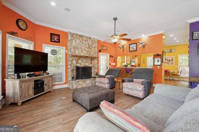 living room with a fireplace, light hardwood / wood-style floors, crown molding, and ceiling fan