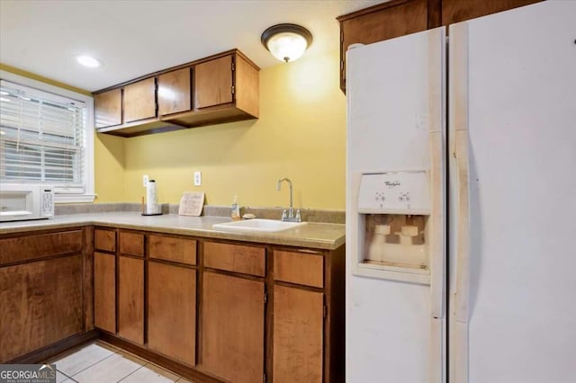 kitchen with white appliances, brown cabinets, light countertops, a sink, and light tile patterned flooring