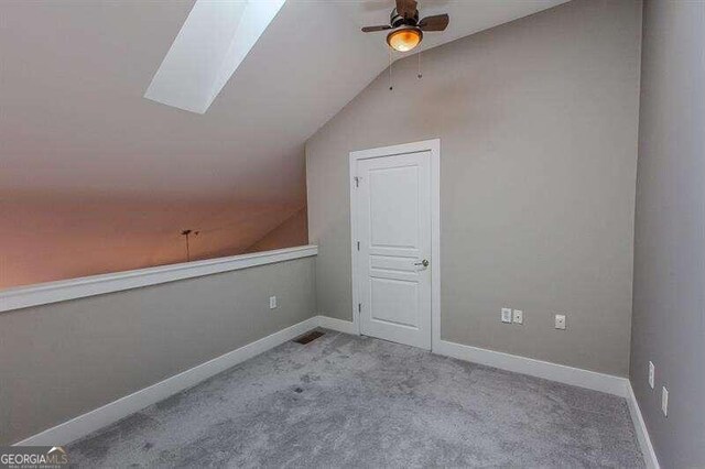 additional living space featuring vaulted ceiling with skylight, carpet, and ceiling fan