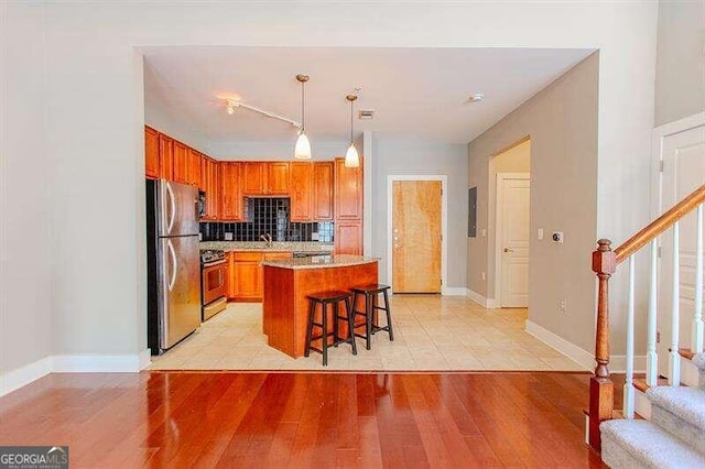 kitchen with range, stainless steel refrigerator, light wood-type flooring, backsplash, and a center island