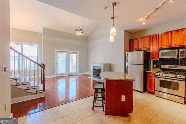 kitchen with tasteful backsplash, stainless steel appliances, track lighting, lofted ceiling, and light tile patterned flooring