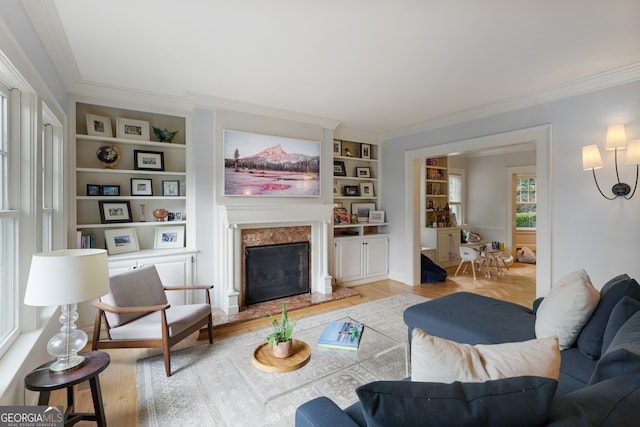 living room featuring built in shelves, light hardwood / wood-style flooring, ornamental molding, and a high end fireplace