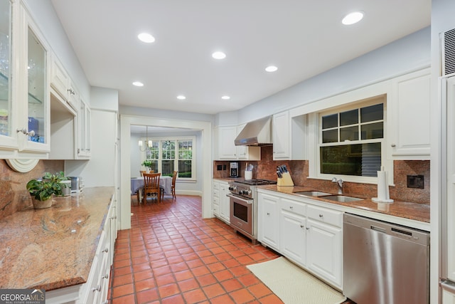 kitchen with stainless steel appliances, white cabinets, wall chimney range hood, sink, and backsplash