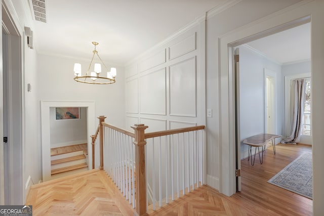 staircase featuring crown molding, a notable chandelier, and light parquet flooring